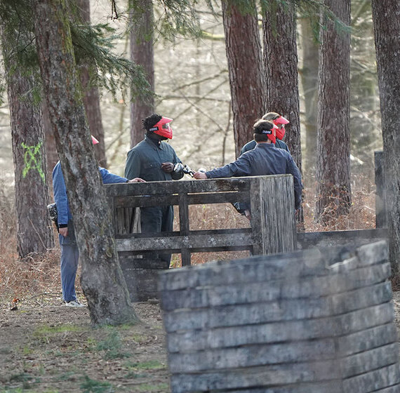 Joueurs de paintball avec masques rouges en position stratégique derrière une barricade en bois dans une forêt de pins à Wavre