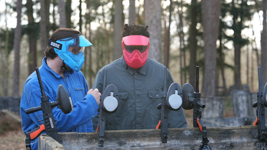 Deux joueurs de paintball équipés de masques de protection bleu et rouge tenant leurs marqueurs avant une partie en forêt à Ottignies