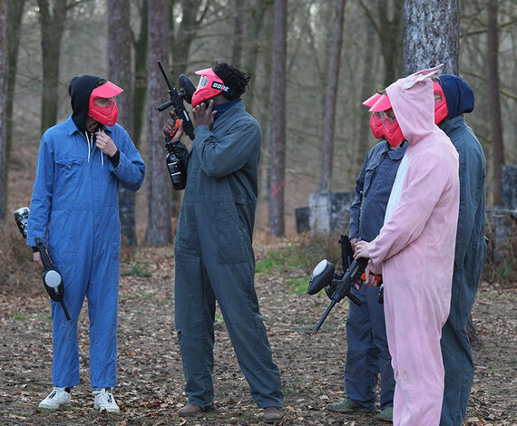 Groupe de joueurs équipés de combinaisons et lanceurs paintball discutant en forêt avant une partie près de Louvain-la-Neuve